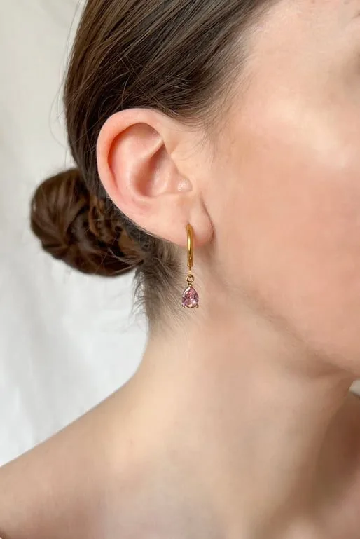 Photo porté des boucles d'oreilles personnalisables Chic rose. Pendentif en forme de goutte doré et en acier inoxydable, de petite taille, orné d’un zircon rose.