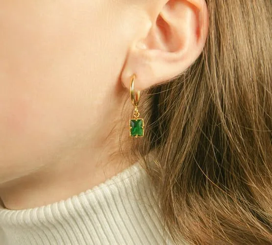 Photo porté des boucles d'oreilles personnalisables Divine vert. Pendentif doré et en acier inoxydable en forme de carré, de petite taille, orné d'un zircon vert.