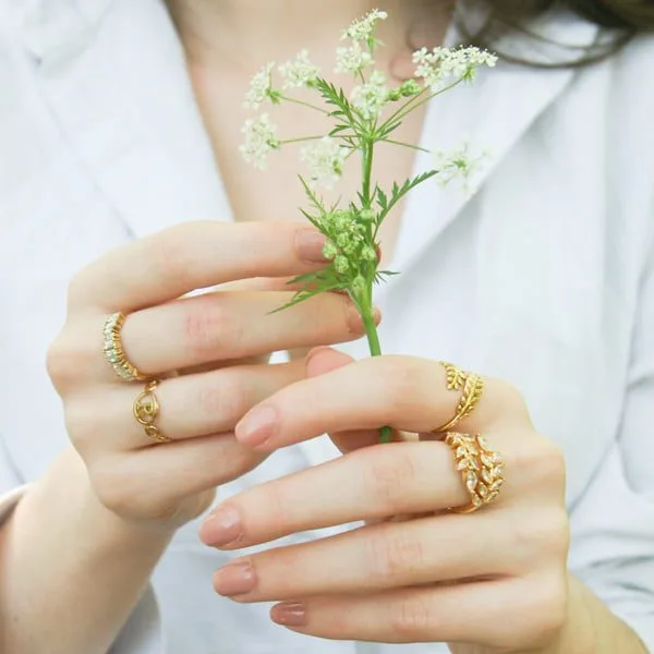 Photo d'une femme tenant dans ses mains des petites fleurs blanches. Ses mains sont habillées par les bagues Laurier, Sparkling, Initial et Royal blanc.